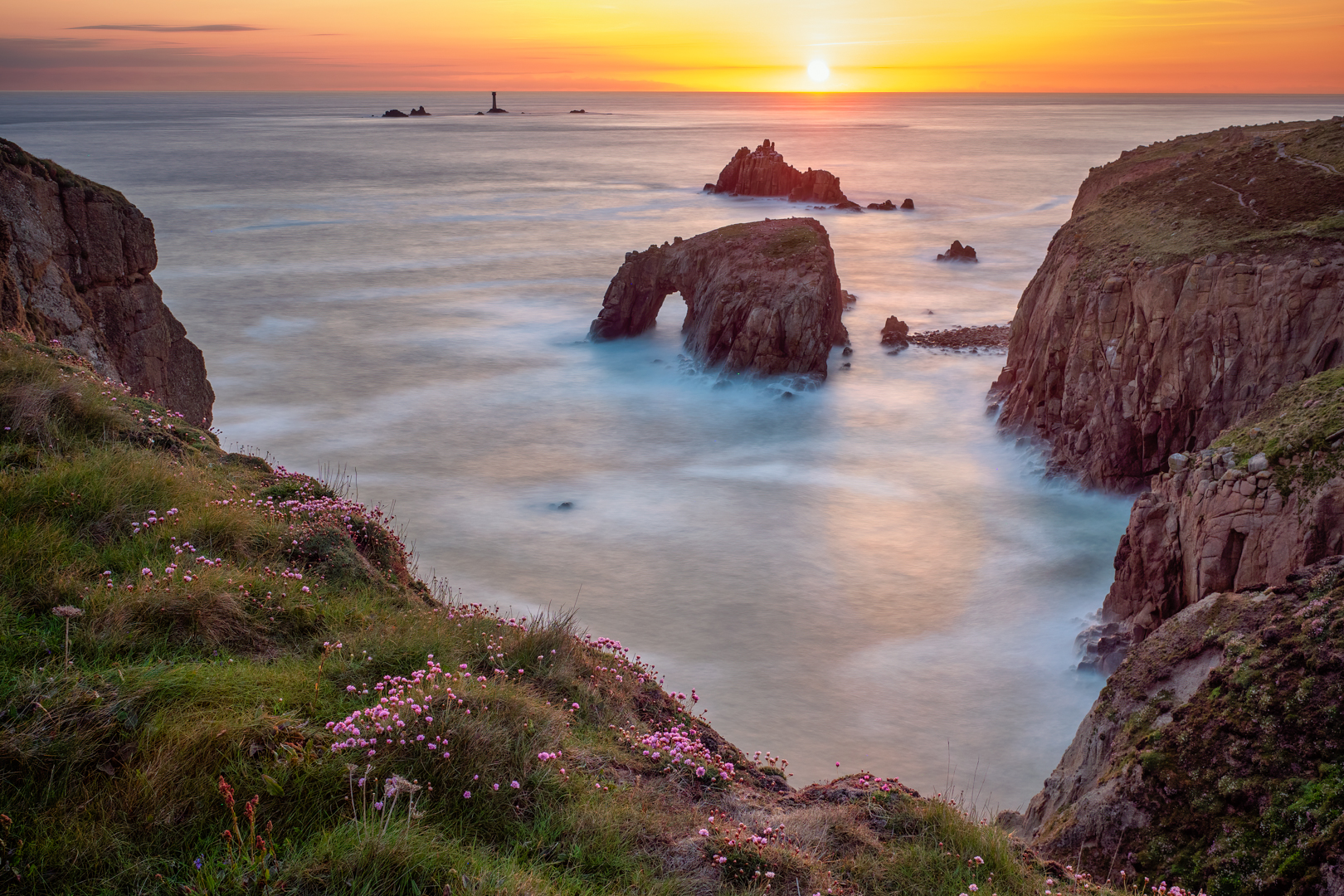 seascape at sunset with a stone arch and lighthouse by photographer Eric Drumm